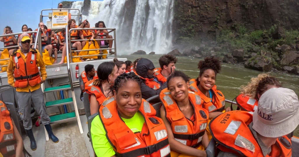 Students on a boat with bright orange life vests visiting Iguazu Falls. 