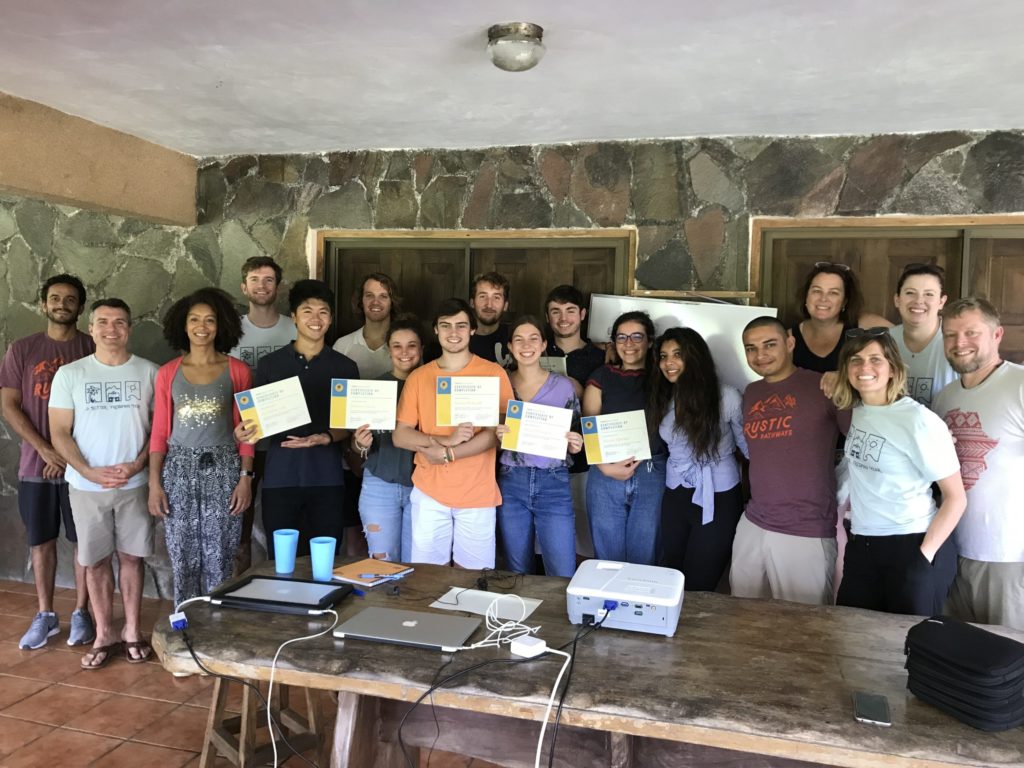 Verto Education students and staff celebrating program completion with certificates in a rustic stone classroom abroad