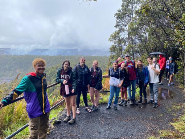 Smiling students stand in the rain with the beautiful scene of Volcano National Park in Hawaii
