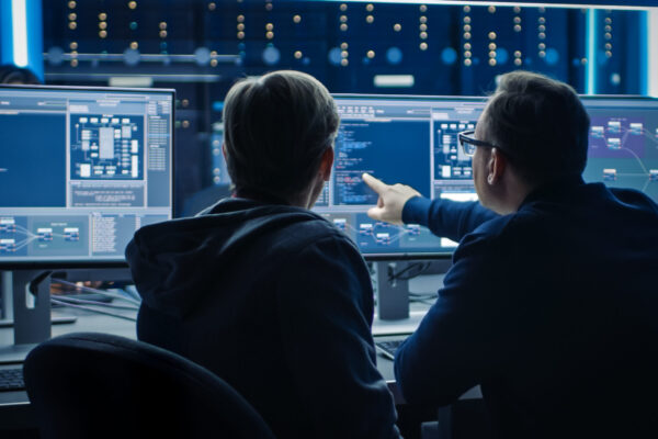 Two Professional IT Programers Discussing Blockchain Data Network Architecture Design and Development Shown on Desktop Computer Display. Working Data Center Technical Department with Server Racks