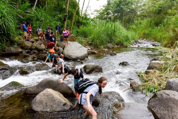 A group of students carefully cross a rushing river.