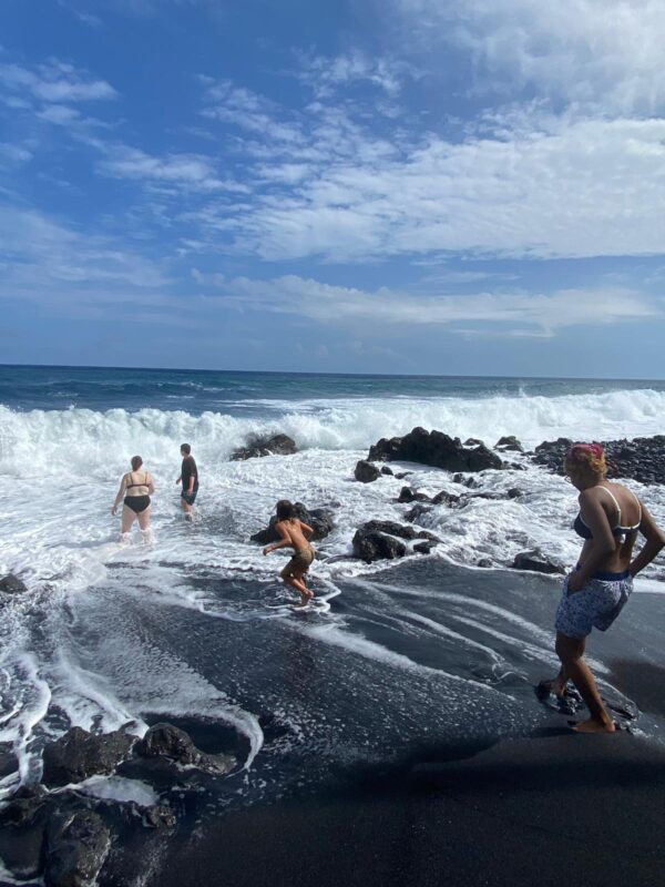 Students play in the water of a Hawaiian black sand beach.