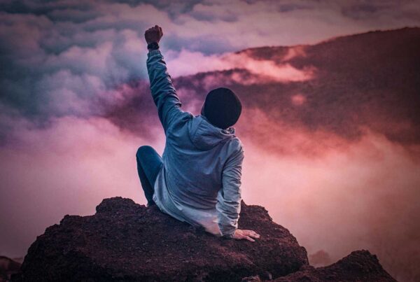 Photo: A student celebrates at the top of a mountain peak