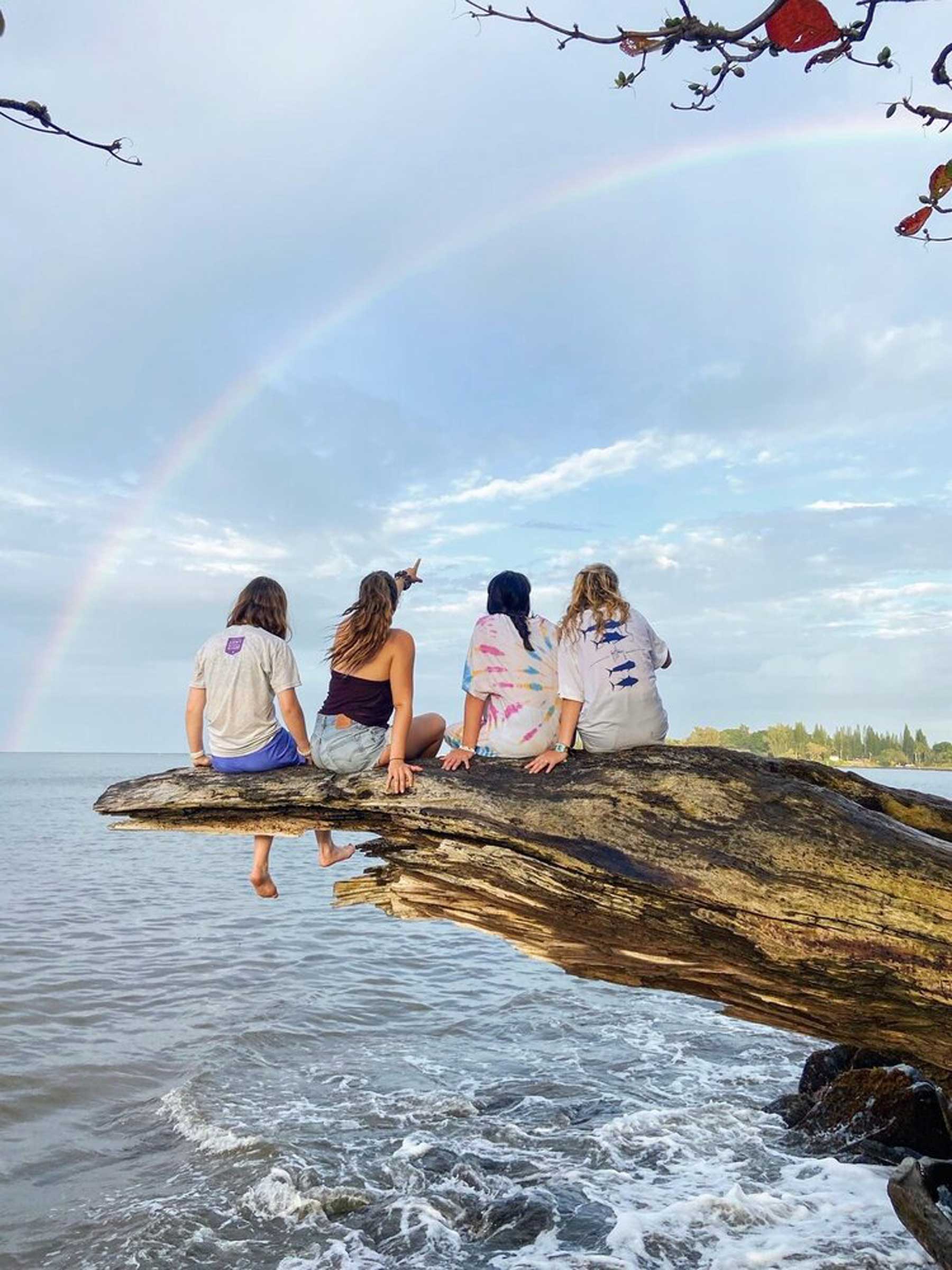 Photo: Verto Education students sitting on driftwood viewing rainbow over ocean
